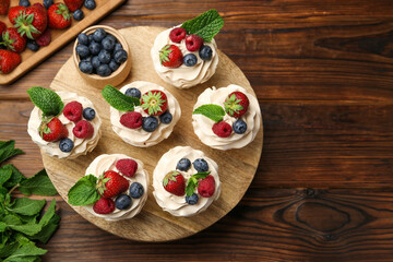 Tasty cupcakes with different berries and mint on wooden table, flat lay. Space for text