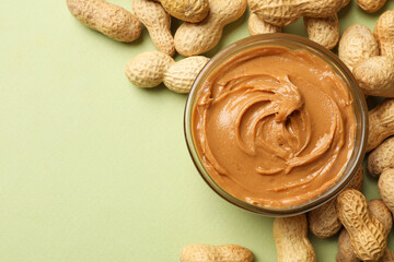 Tasty peanut butter in bowl and groundnuts on pistachio color background, flat lay. Space for text