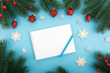 Spruce branches, red berries, Christmas tree toys, snowflakes and a notebook on a blue background