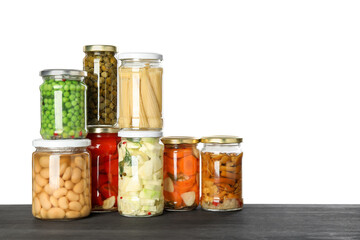 Different pickled products in jars on dark wooden table against white background. Space for text
