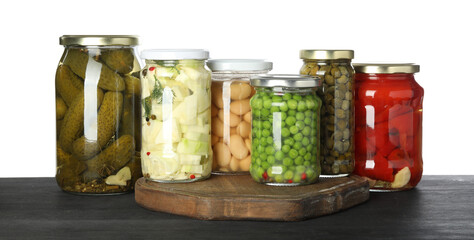 Different pickled products in jars on dark wooden table against white background