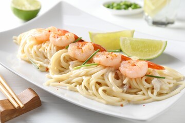 Delicious pasta with shrimps, green onions, lime and chopsticks on white wooden table, closeup