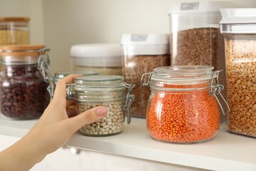 Woman with containers of different cereals and legumes in kitchen, closeup