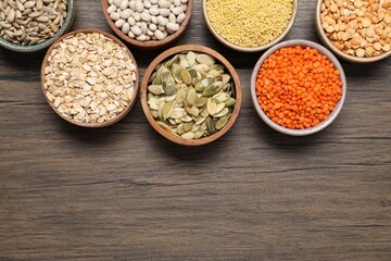 Different types of cereals, seeds and legumes in bowls on wooden table, flat lay. Space for text