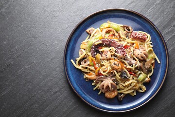 Stir-fry noodles with sea food and vegetables on dark textured table, top view. Space for text