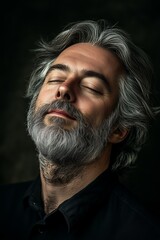 A serene man with gray hair and a beard enjoying a moment of calm against a dark background in a peaceful atmosphere