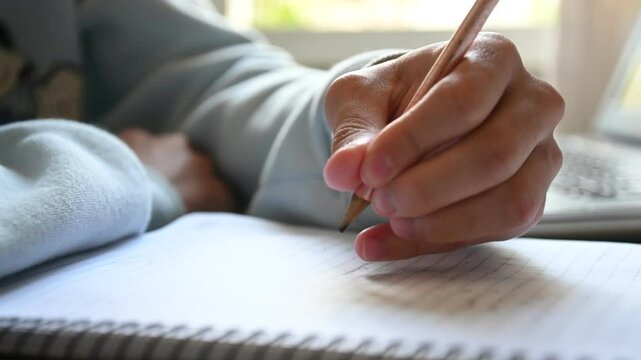 Detalhe de m&atilde;o de estudante escrevendo no caderno na bancada de estudos. 