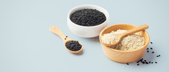White sesame in wooden bowl with black sesame seeds on light blue background