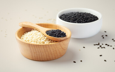 Sesame seeds in wood bowl with spoon, white and black sesame on beige background