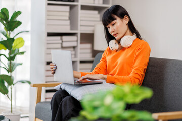 A young woman of asian descent wearing headphones, deeply focused while sitting at her desk with a...