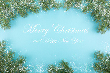 Green spruce branches in the snow ona blue background. Postcard, Merry Christmas and New Year greetings.