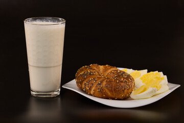 a plate with sliced ​​boiled eggs, pretzels and kefir on a black background