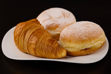 donuts filled with jam and a croissant on a white plate on a black background