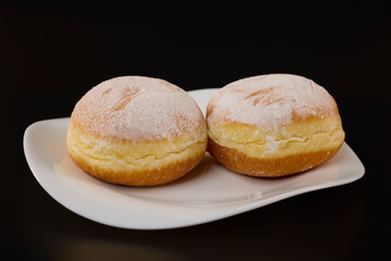 two donuts filled with jam on a white plate on a black background