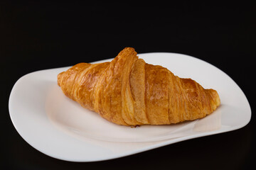 croissant with butter on a white plate with a black background
