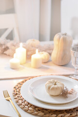 Thanksgiving day table setting with fall decorations, centerpiece of colorful flowers in pumpkin as vase on white table. Close up. Vertical format.