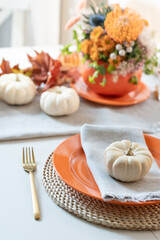 Thanksgiving day table setting with fall decorations, centerpiece of colorful flowers in pumpkin as vase on white table. Close up. Vertical format.