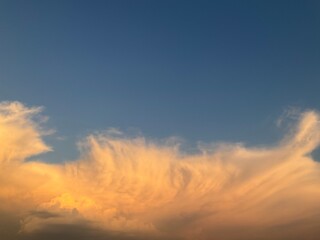 Sky background with blue color and stormy menacing Anvil cloud, Cumulonimbus incus illuminated in orange by sunlight at the evening. Topics: storm alert, meteorology, weather, nature, climate