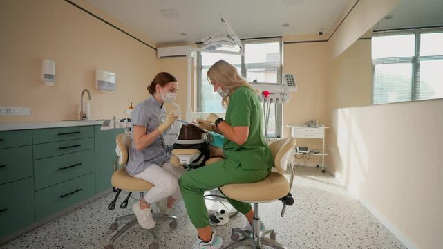 Blonde Woman Dentist with Assistant Treat Teeth of Female Patient with Special Instrument. Treatment of Caries and Plaque in Dental Clinic. Concept of Medicine and Healthcare. Slow Motion.