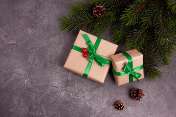 Gifts in boxes with green ribbons, fir branches and cones on a gray background. Postcard,...