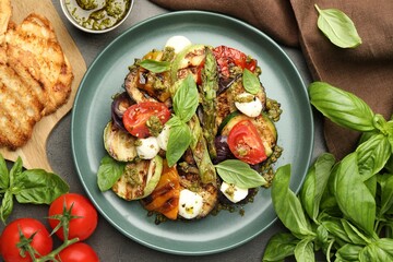 Delicious salad with grilled vegetables, pesto sauce, basil and bread on gray textured table, flat lay
