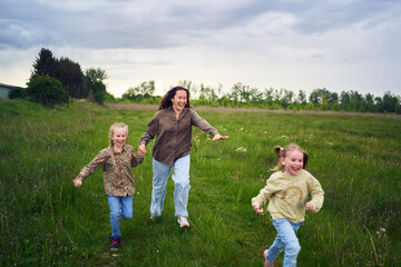 Fototapeta premium mother and children run holding hands in the field
