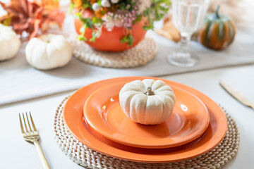 Thanksgiving day table setting with fall decorations, centerpiece of colorful flowers in pumpkin on white table. Festive family dinner at home interior. Close up.