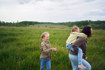 Fototapeta premium a mother rolls her daughters on her back, playing horse, kisses and hugs