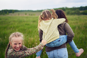 a mother rolls her daughters on her back, playing horse, kisses and hugs