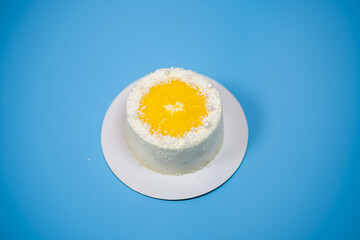 Delicious white cake with orange slice and coconut flakes on blue background