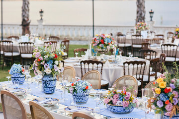 Elegant Outdoor Wedding Reception with Draped Canopy, Floral Centerpieces, and White Chairs Overlooking a Waterfront Venue