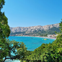 View through the trees of the main beach (Vela Plaza) in Baska on the island of Krk in Croatia