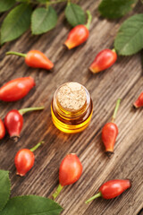 A bottle of rose hip seed oil with fresh rosehips on a table