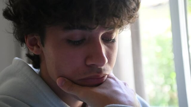 Plano fechado de jovem adulto pensativo na bancada de estudos, fazendo tarefa universit&aacute;ria