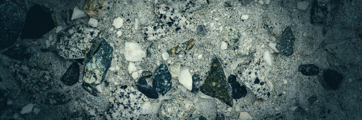 Concrete wall texture with pebbles. Decorative rough concrete surface with white, black and gray stones. Wide panoramic texture for background and design.