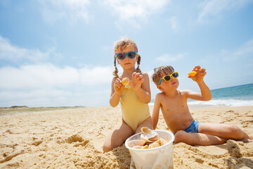 Two happy kids play in sand, wearing shades on bright beach day