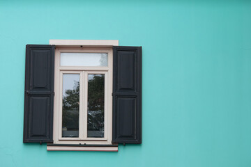 Window with wooden shutters on turquoise wall. Open shutter window. Exterior view of the building. Empty area.