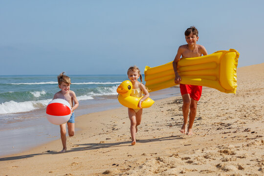 Group of kids playfully race while carry inflatable beach toys