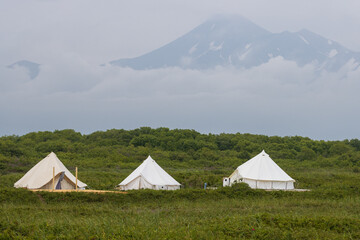 Tent camp on the background of the volcano. View of three large tourist tents. Camping in the wilderness. Travel, tourism and hiking on the Kamchatka Peninsula. Nature of the Far East of Russia.