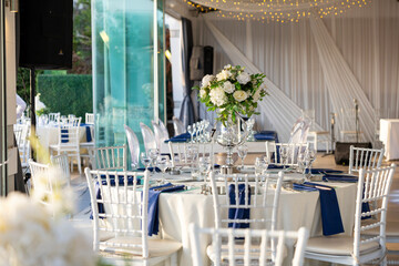 Elegant Outdoor Wedding Reception with White and Blue Floral Centerpieces, Silver Chairs, and...