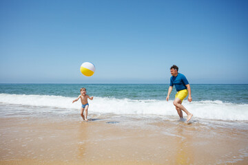 Man and little boy throw a beach ball to each other in waves