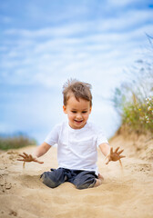 Young child playing joyfully in sandy outdoor area. A cheerful child sits in the sand, happily playing and exploring on a sunny day