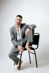 Man in grey costume sits on the chair, barefoot. In studio, fashion