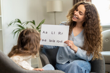 Cute smiling young speech therapist with table with written syllables in hands