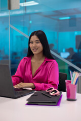 portrait of Young Asian businesswoman working with laptop in modern office with glass wall.