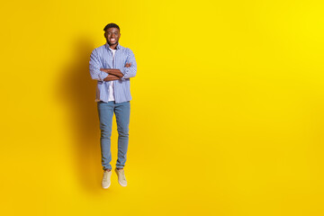 Full length photo of handsome good mood guy wear plaid shirt jumping high arms crossed emtpy space isolated yellow color background