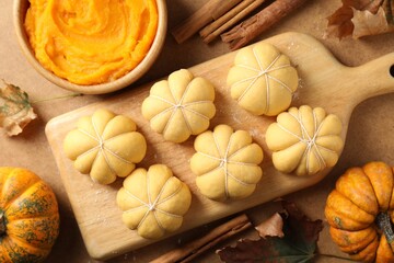 Raw pumpkin shaped buns and ingredients on brown table, flat lay