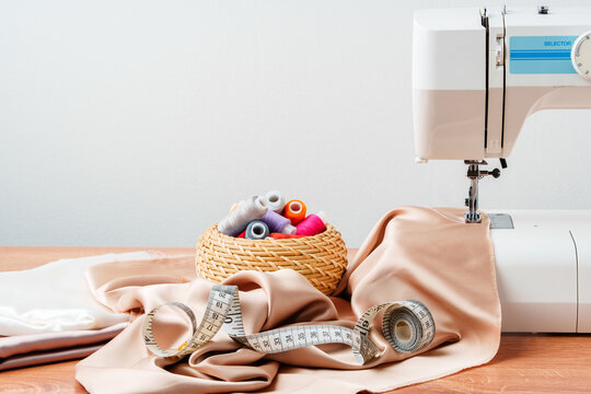 A sewing machine on a wooden table with fabric and thread organized in a basket