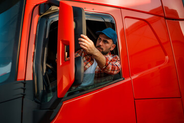 Caucasian truck driver adjusting the side mirror of a bright red truck.
