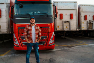 Naklejka premium Proud truck company owner standing in front of his truck with hands in pocket and smiling for the photo.
